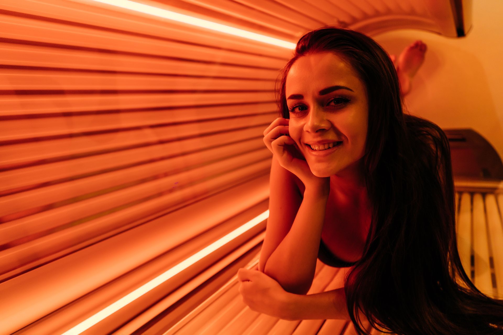 A woman is laying in a tanning bed with red lights.