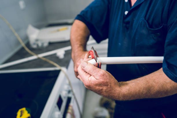 Plumber cutting plastic pipe with red cutter during kitchen plumbing installation.