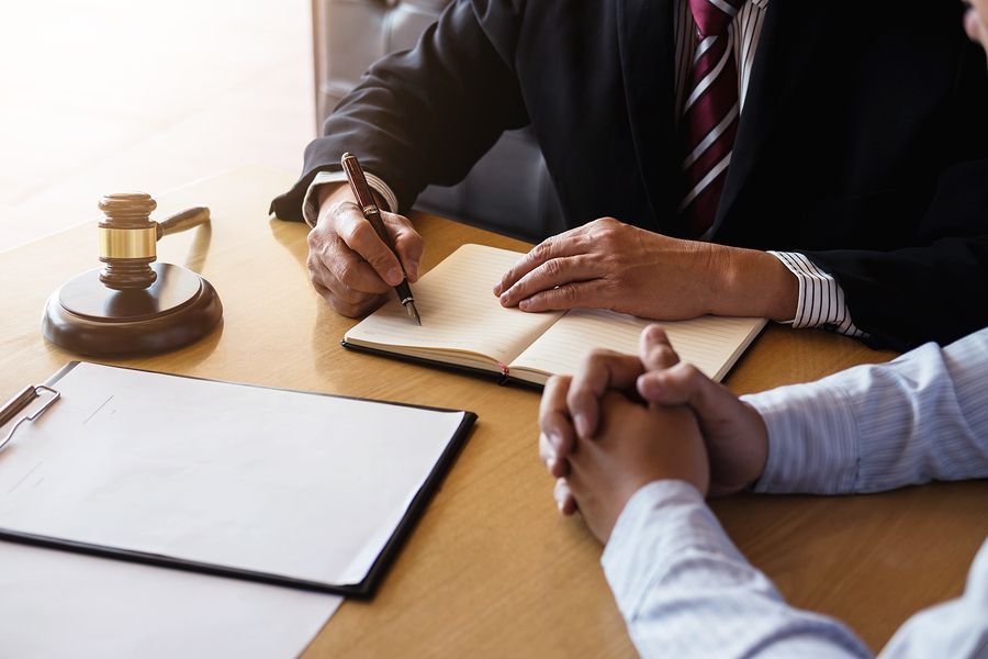 A lawyer is sitting at a table with a client and writing in a notebook.