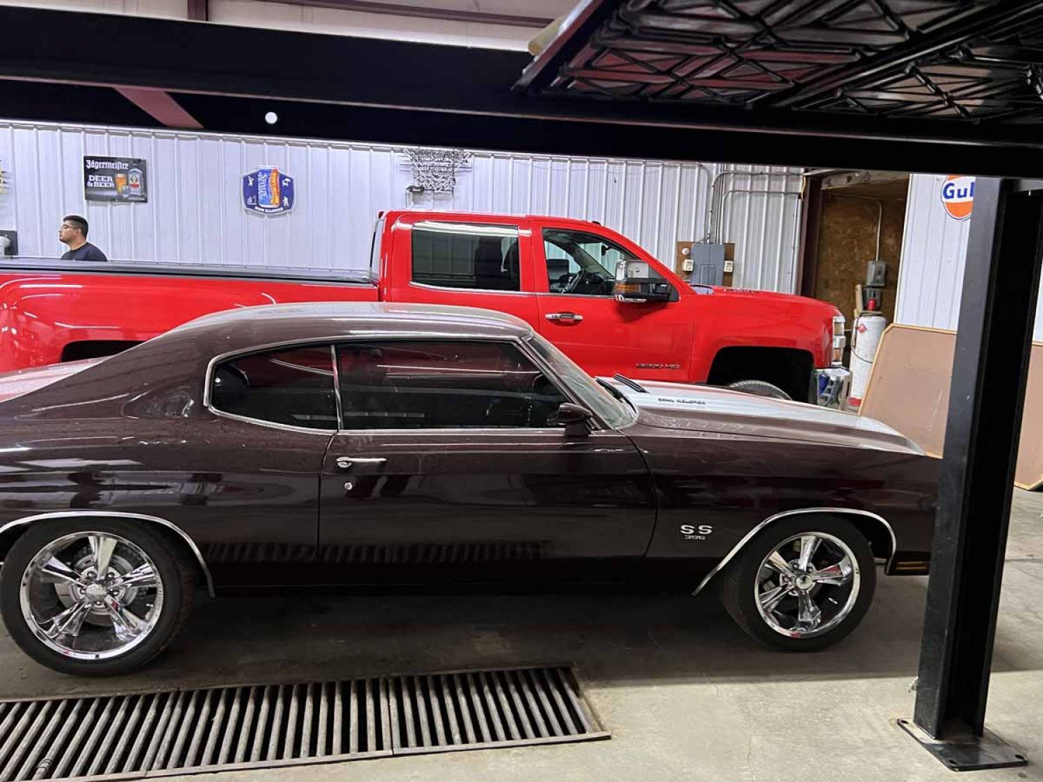 A red truck is parked next to a brown car in a garage.