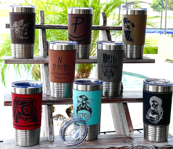 A display of stainless steel tumblers with leather sleeves on a wooden table.