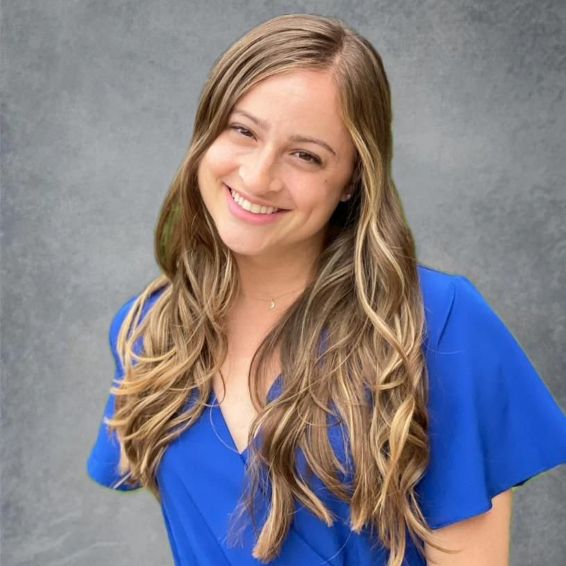 A woman with long hair is wearing a blue shirt and smiling.