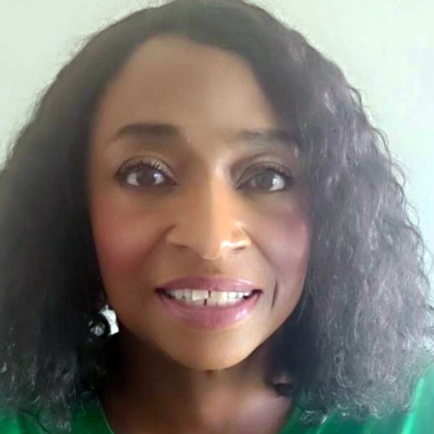 A woman with curly hair is smiling and wearing a green shirt.