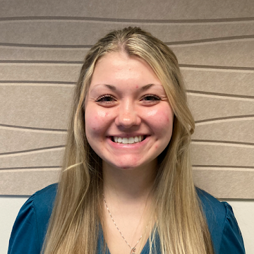 A woman with curly hair is smiling and wearing a green shirt.
