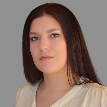 A woman with long dark hair is wearing a white shirt and looking at the camera.