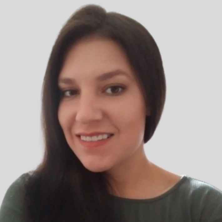 A woman with long dark hair is wearing a white shirt and looking at the camera.