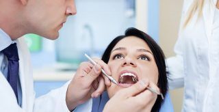 A woman is sitting in a dental chair while a dentist examines her teeth.