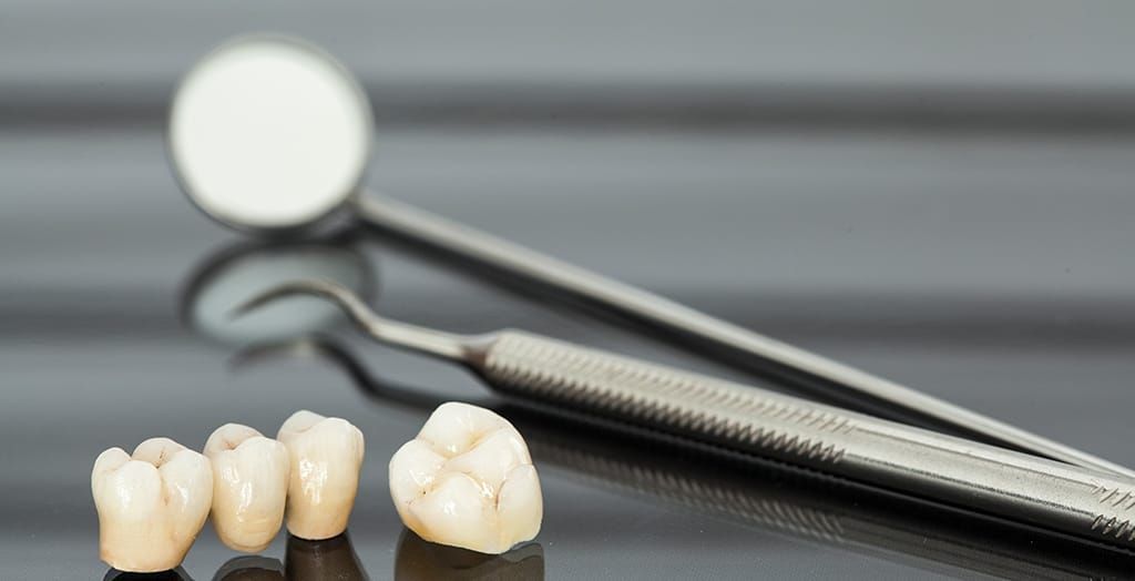 Three dental crowns and a dental mirror on a table.