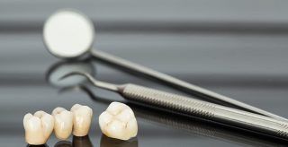 A dental mirror , tweezers , and dental crowns on a table.