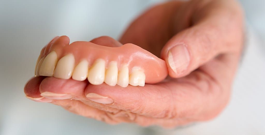 A person is holding a full denture in their hand.