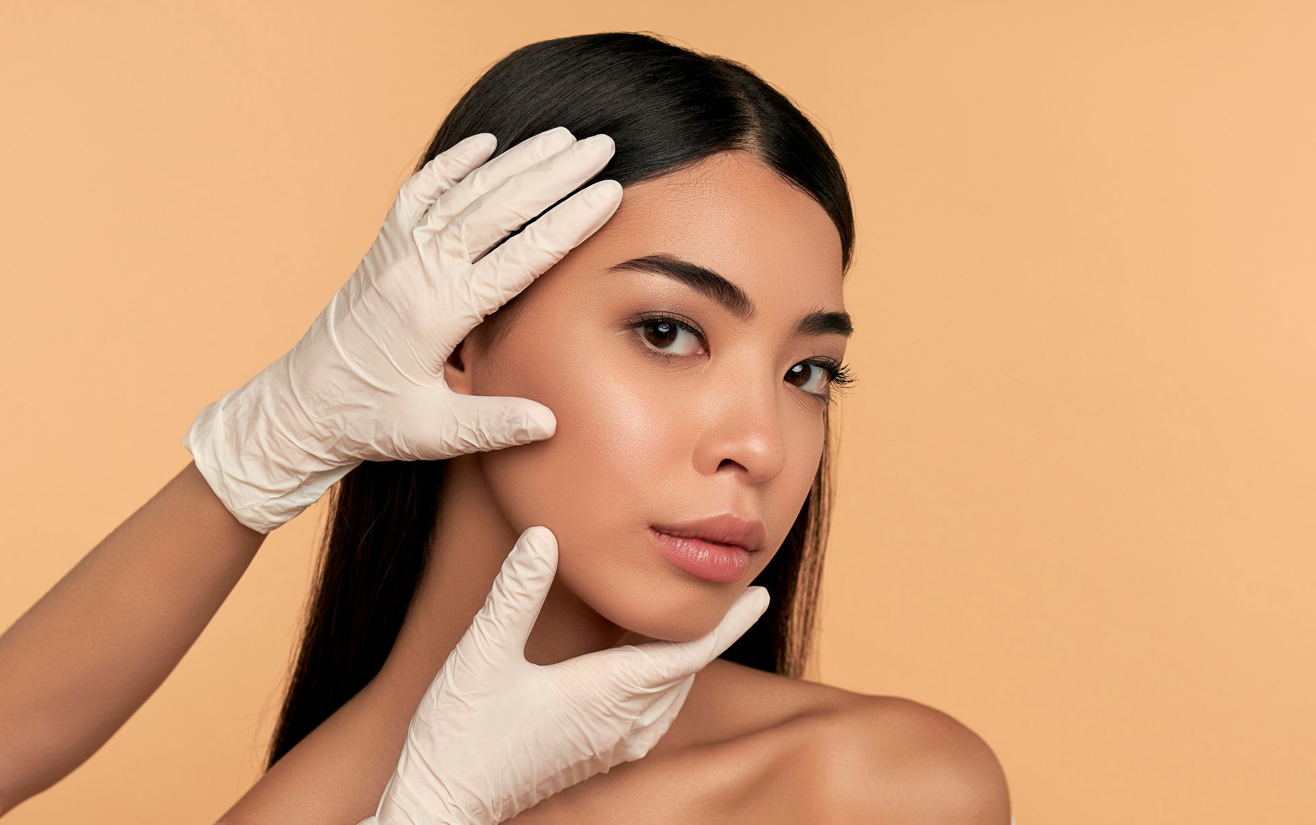 A woman is getting her face examined by a doctor wearing gloves.