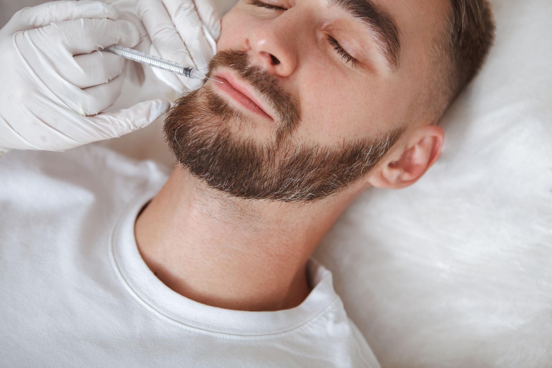 A man with a beard is getting a botox injection in his face.