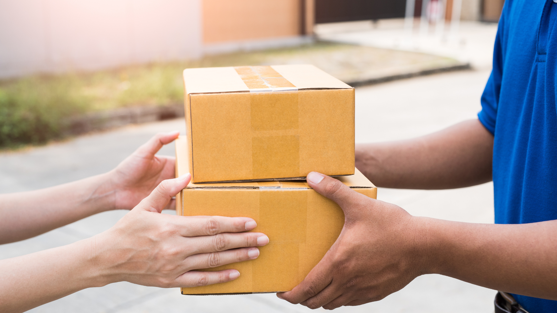 Delivery person hands two cardboard boxes to a person outside a building.