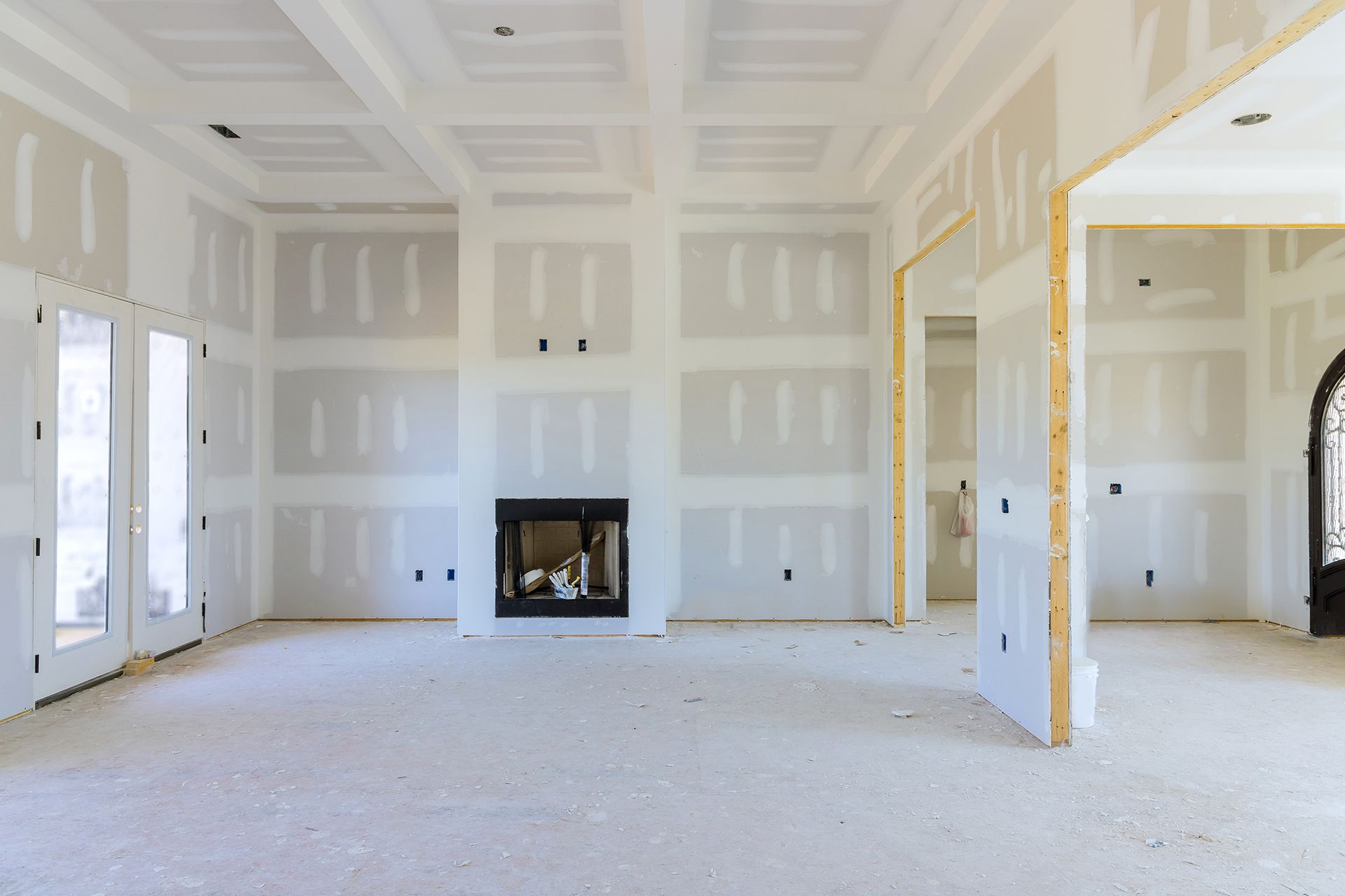 Interior of a room under construction with drywall installed on walls and ceiling, a fireplace, and doorway openings.