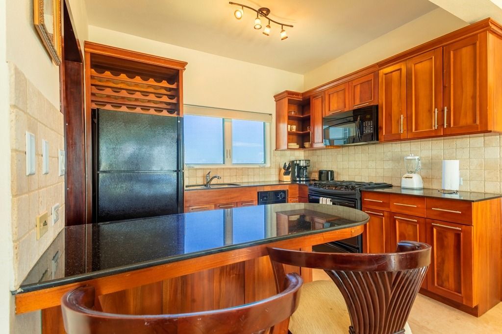 Kitchen with wooden cabinets, dark countertops, and a black refrigerator.