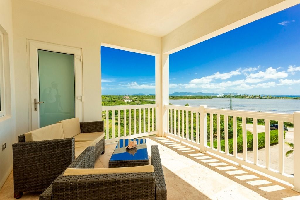 Balcony with wicker furniture, white railings, and a view of blue sky and water.