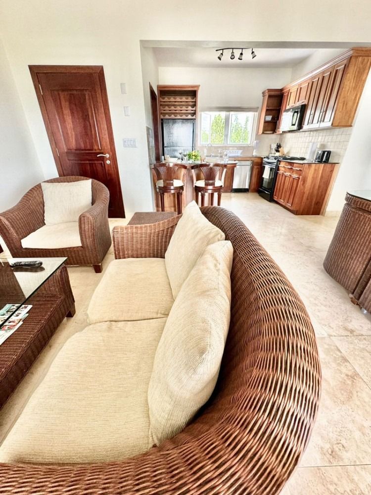 Living room with wicker furniture, open to a kitchen with wooden cabinets.