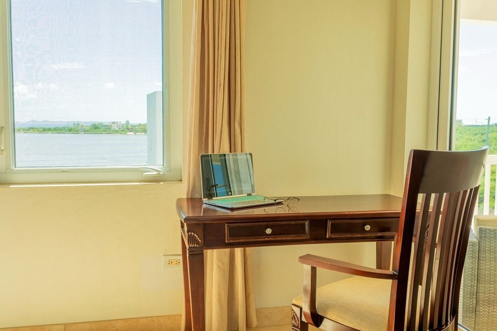 Desk with open laptop and chair by a window overlooking water.