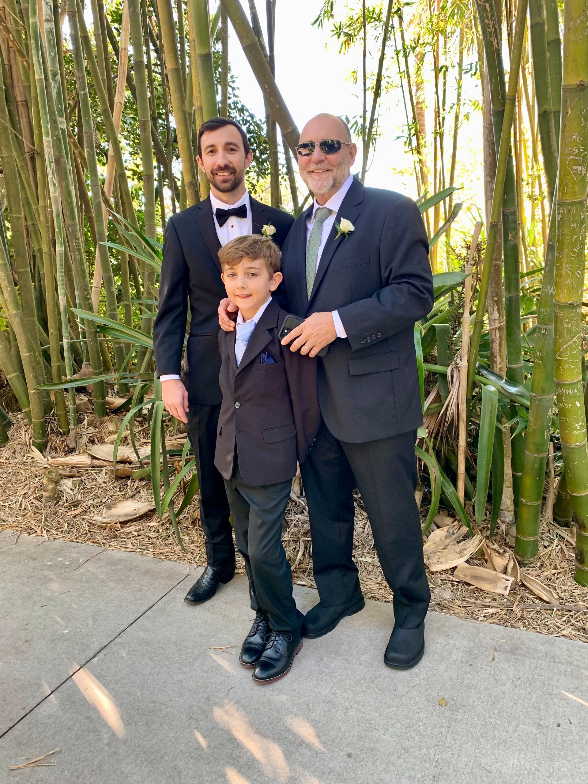 Three men in suits are posing for a picture in front of a bamboo forest.