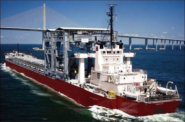 A large ship is floating in the ocean under a bridge