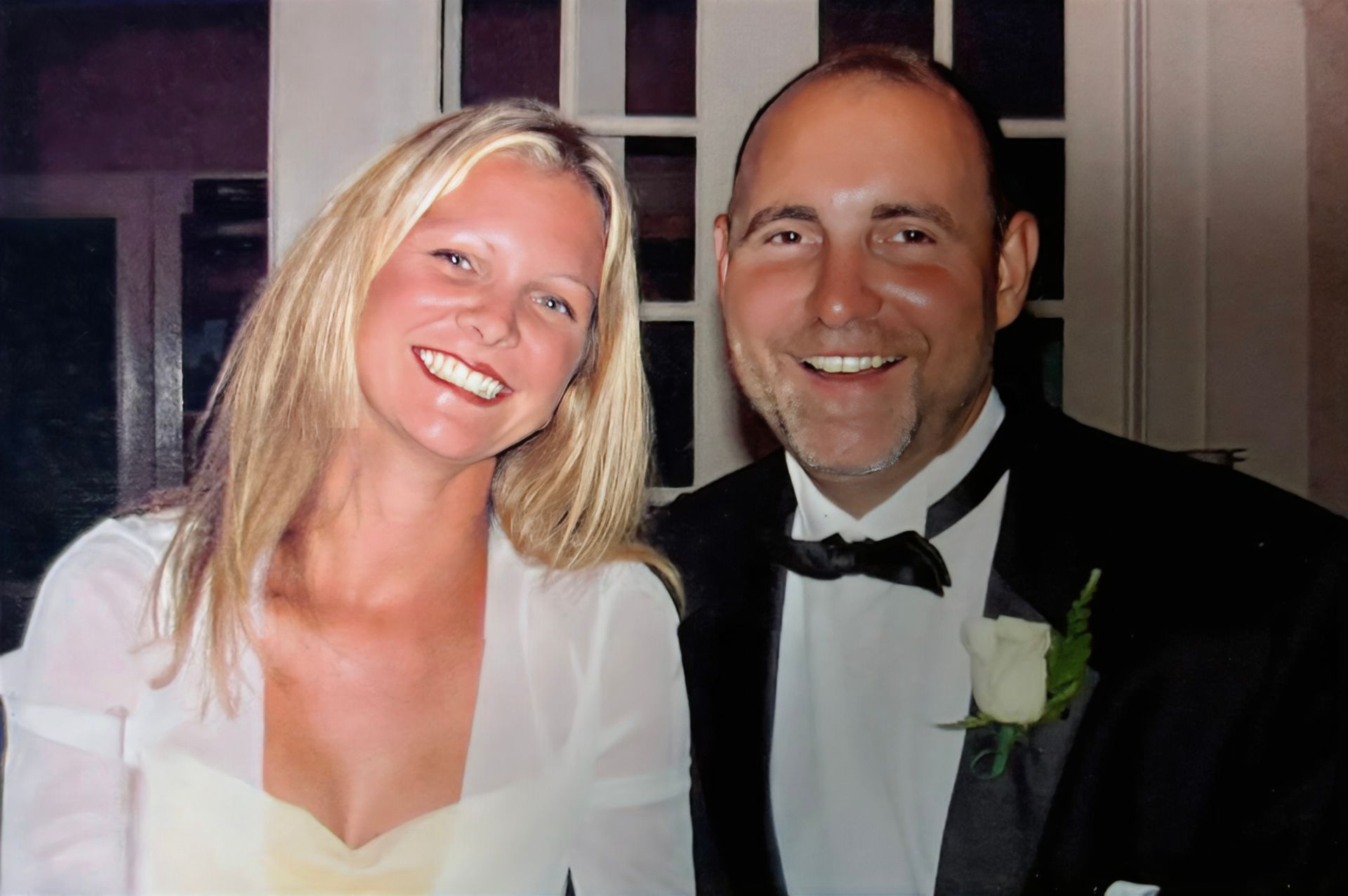A man in a tuxedo and a woman in a white dress pose for a picture