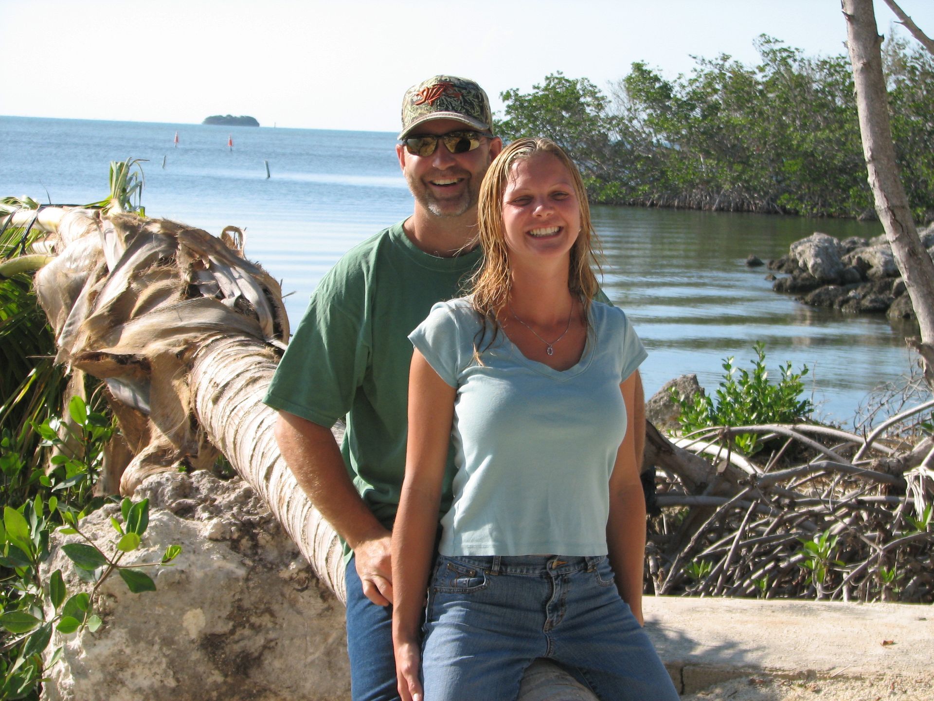 A man and a woman pose for a picture in front of a body of water