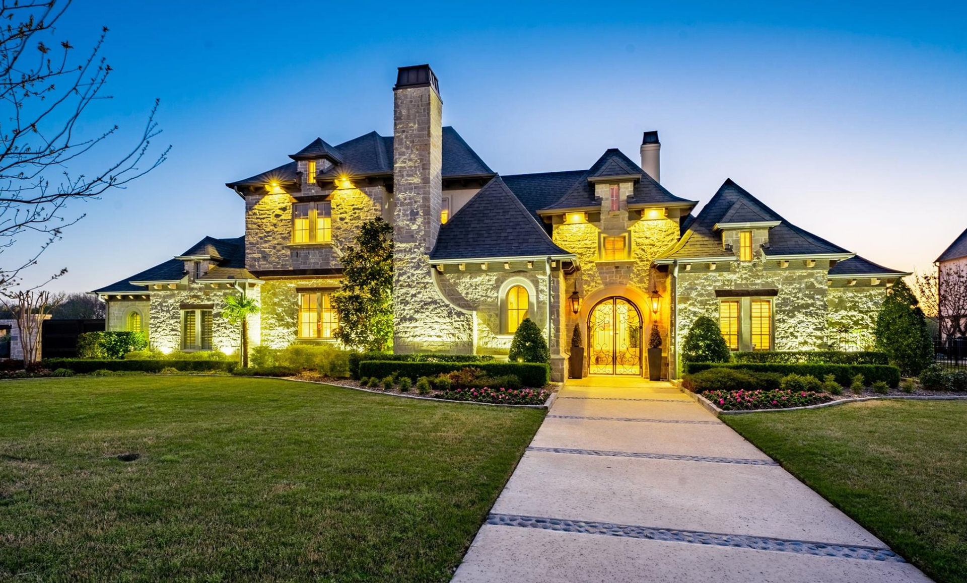 A large stone house with a driveway leading to it is lit up at night.