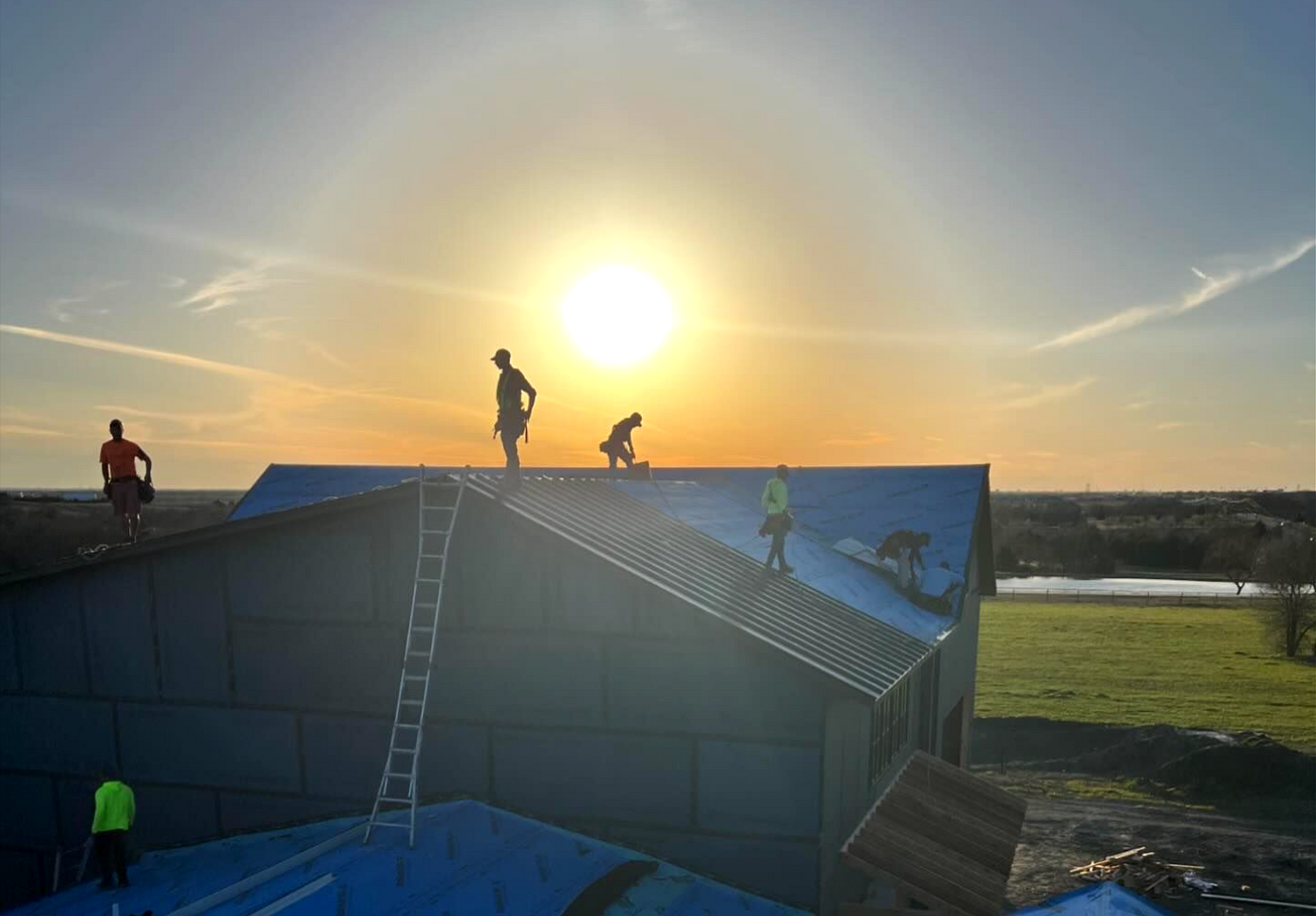 A group of people are working on the roof of a building at sunset.