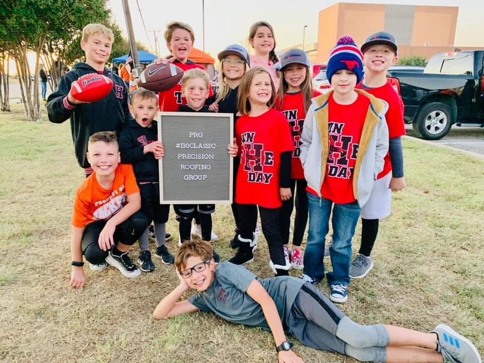 A group of children are posing for a picture while holding footballs and a sign.