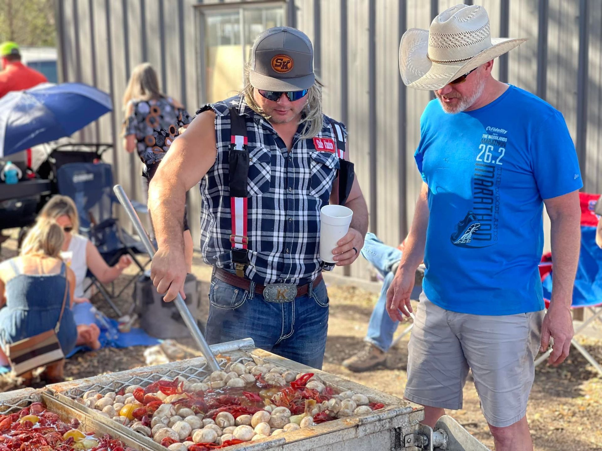 Two men in cowboy hats are standing around a table cooking food.