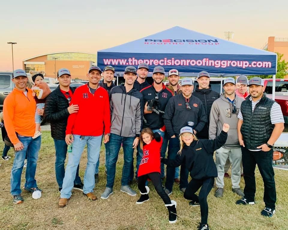 A group of people are posing for a picture under a tent that says the precision roofing group.