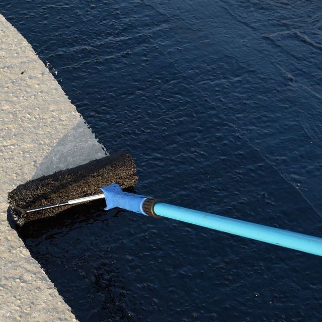 A roller with a blue handle is being used to paint a concrete surface