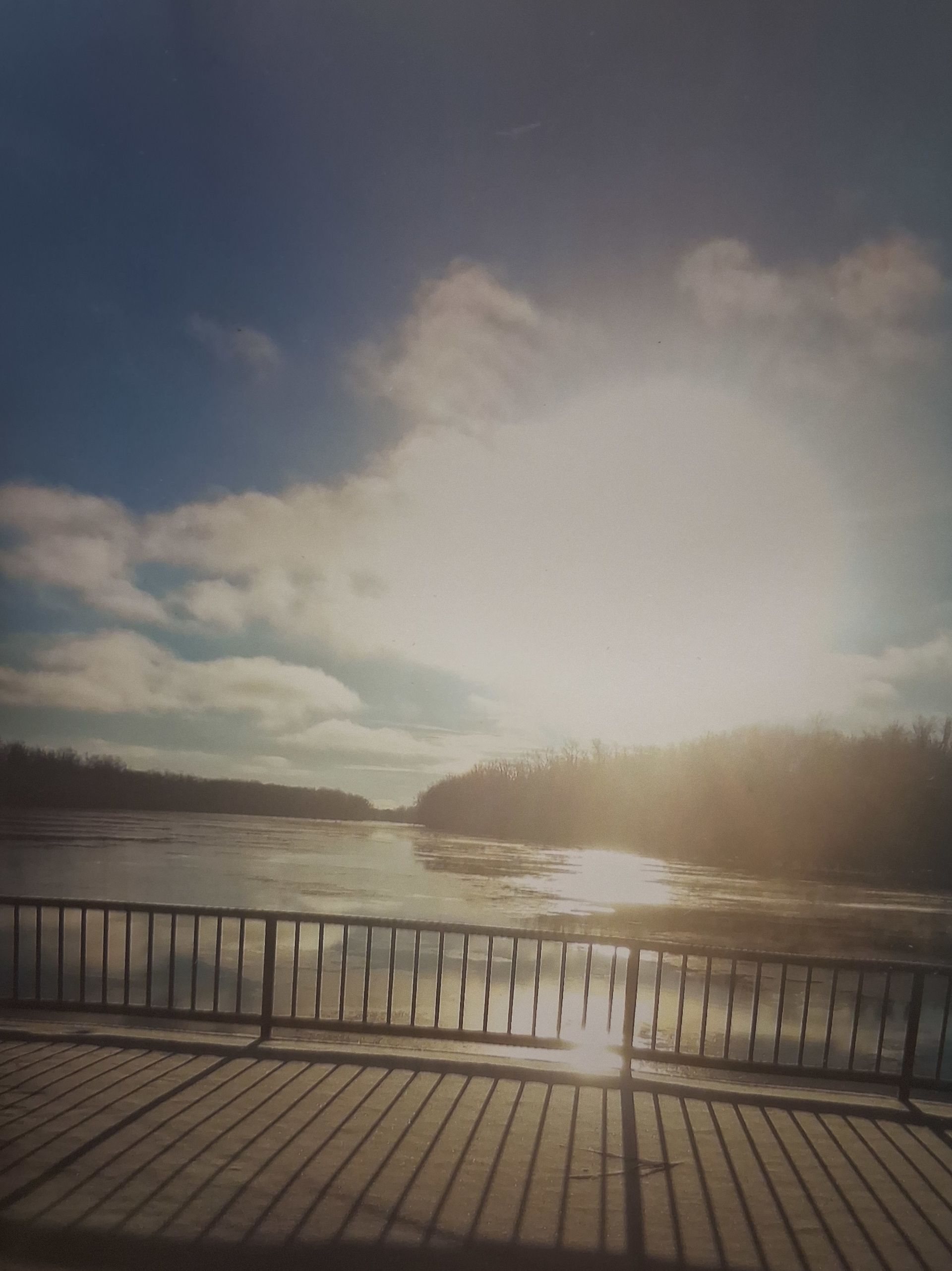 Bridge over a river with bright sunlight. The sky is partly cloudy.
