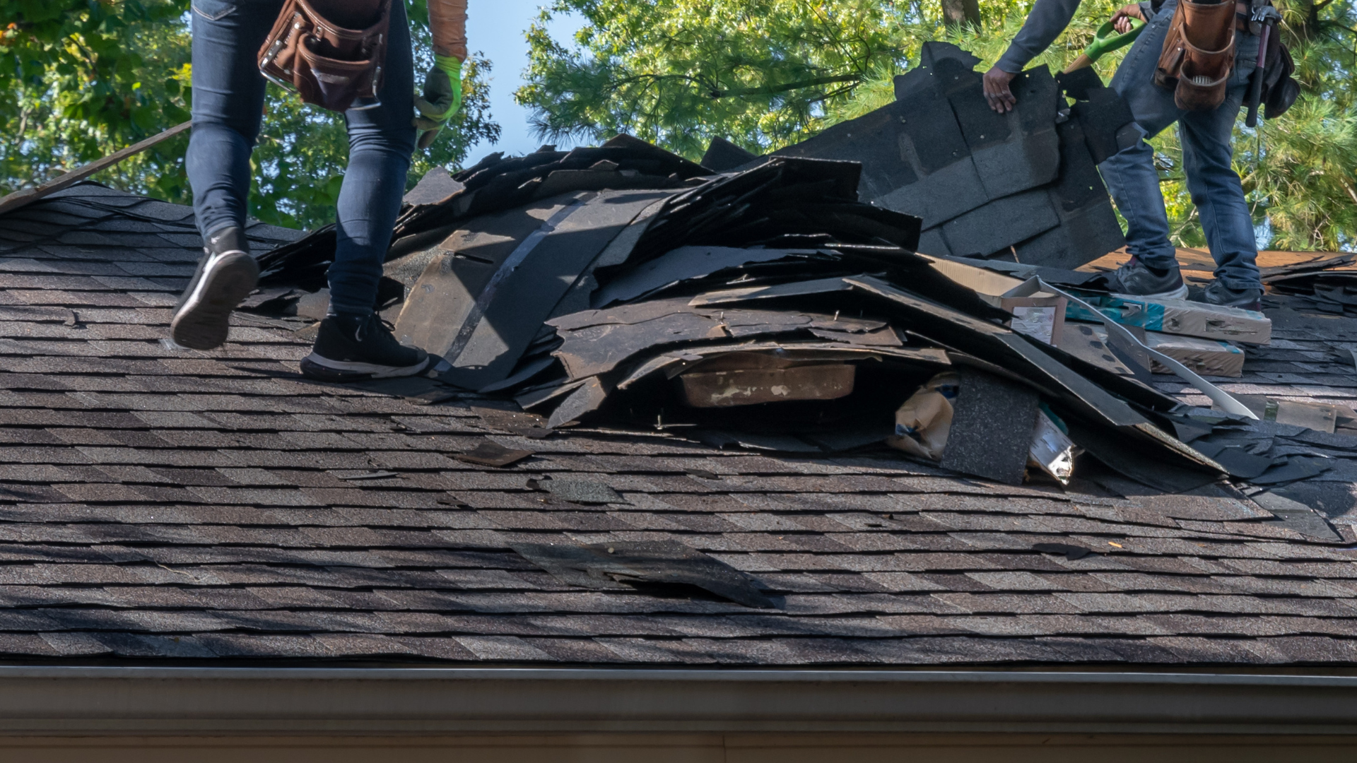 Roofers removing old asphalt shingles from a residential roof.