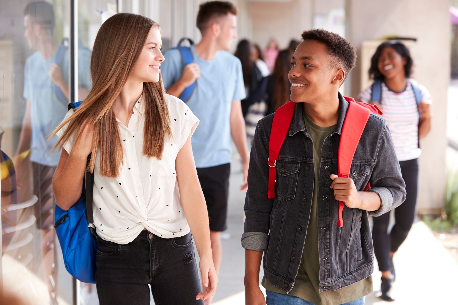 A boy and a girl are walking down a hallway and talking to each other.