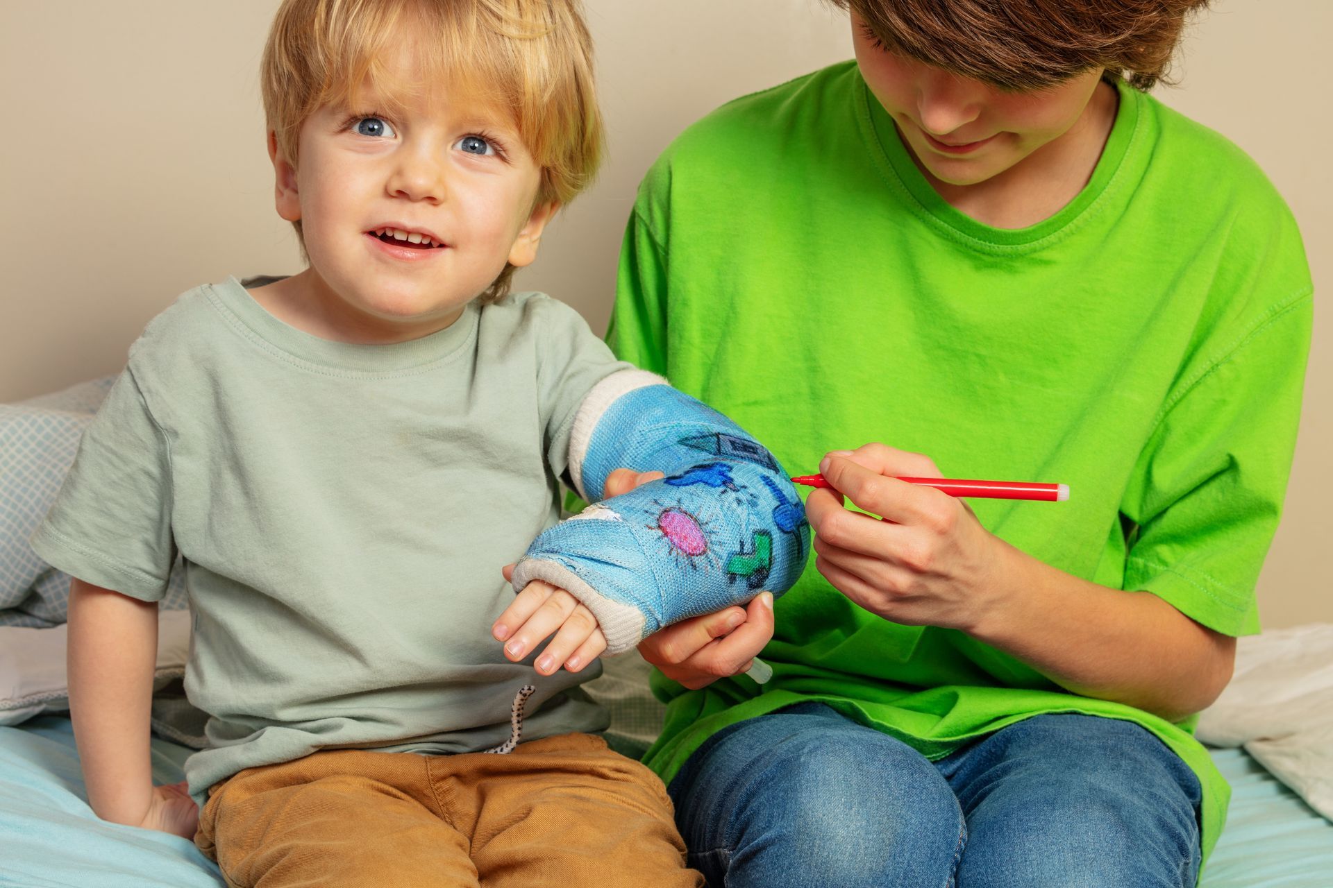 A boy is painting a cast on a little boy 's arm.