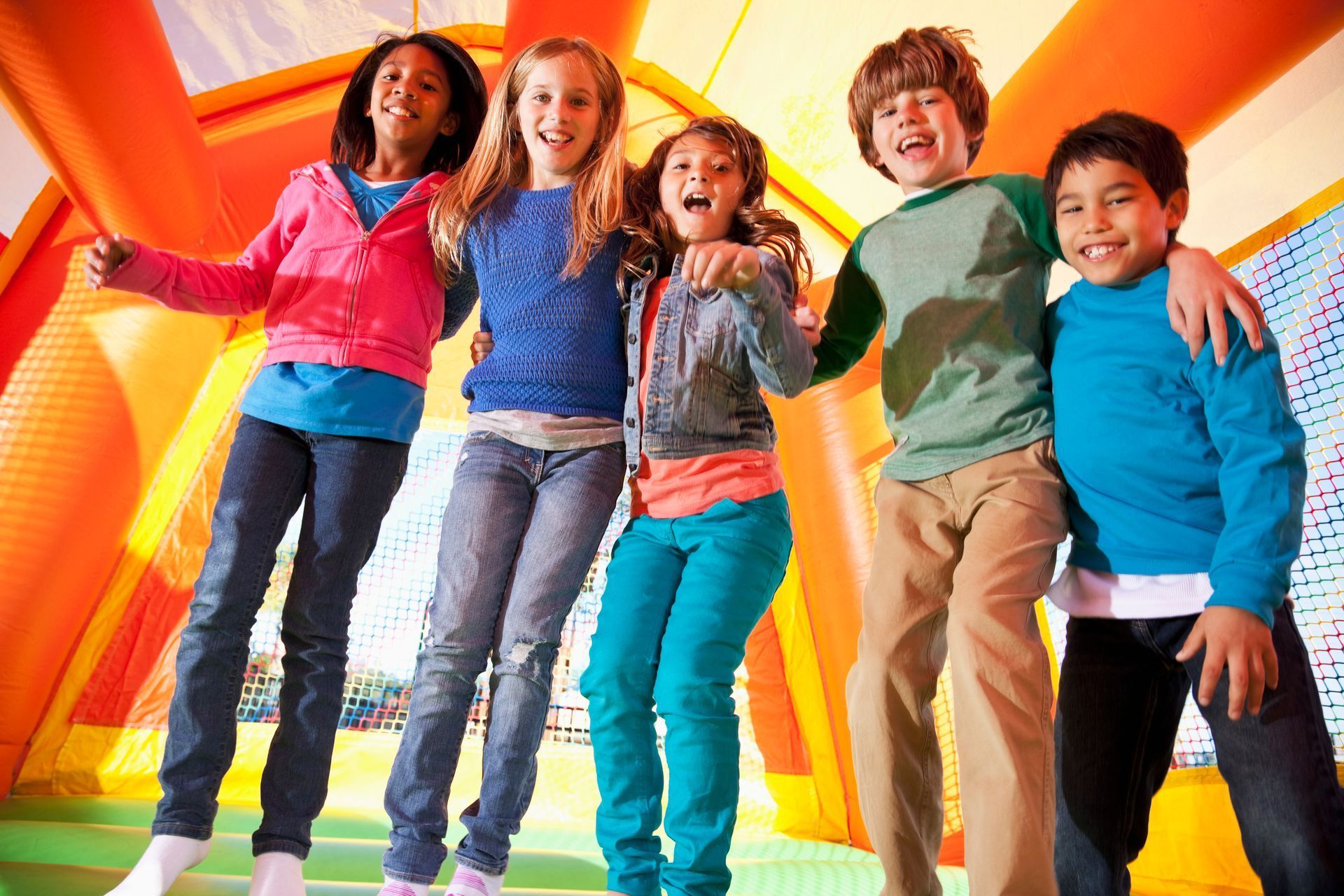 Children standing inside a colorful bouncy house. They have their arms around each other's shoulders and are smiling.