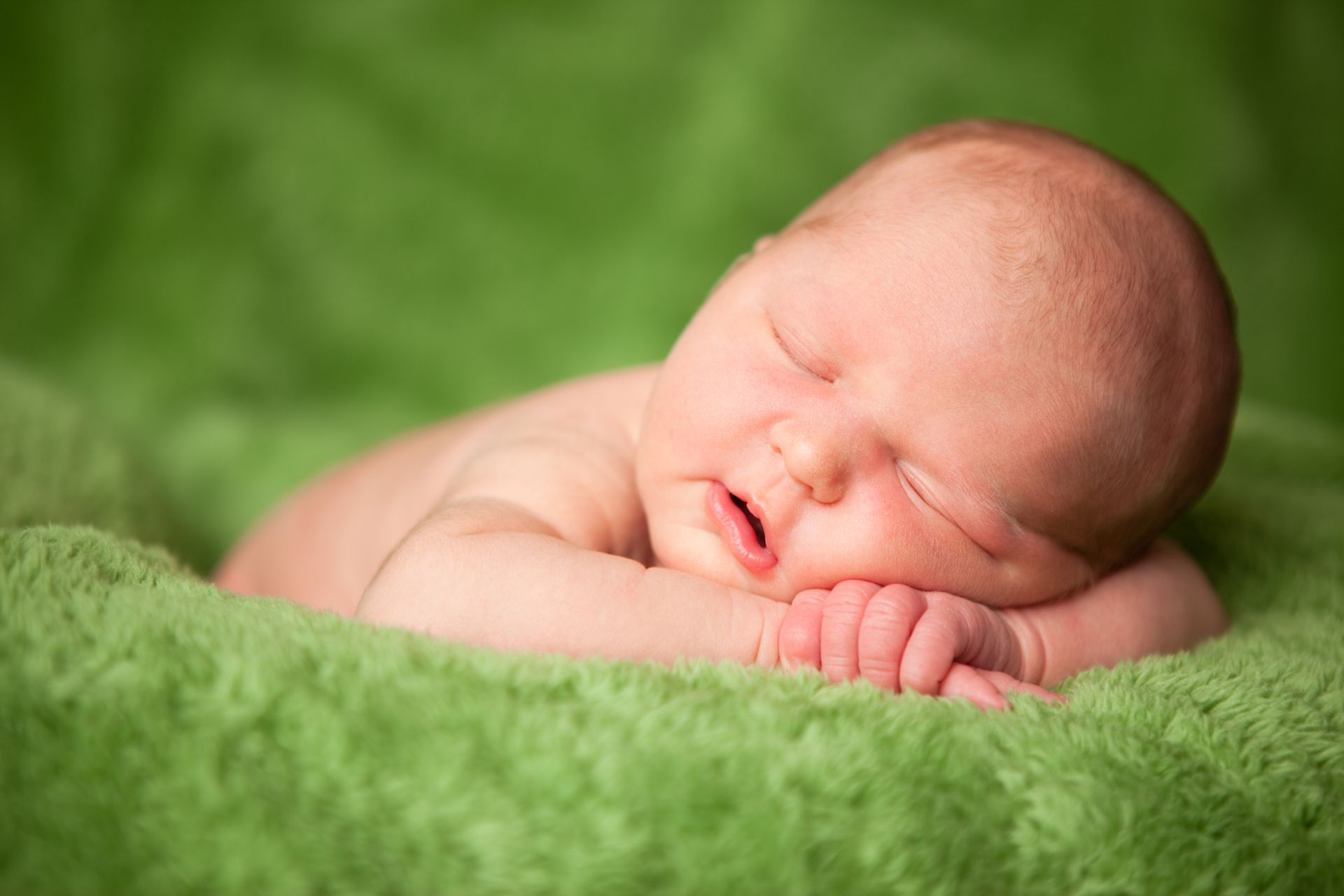 A newborn baby is sleeping on a green blanket.