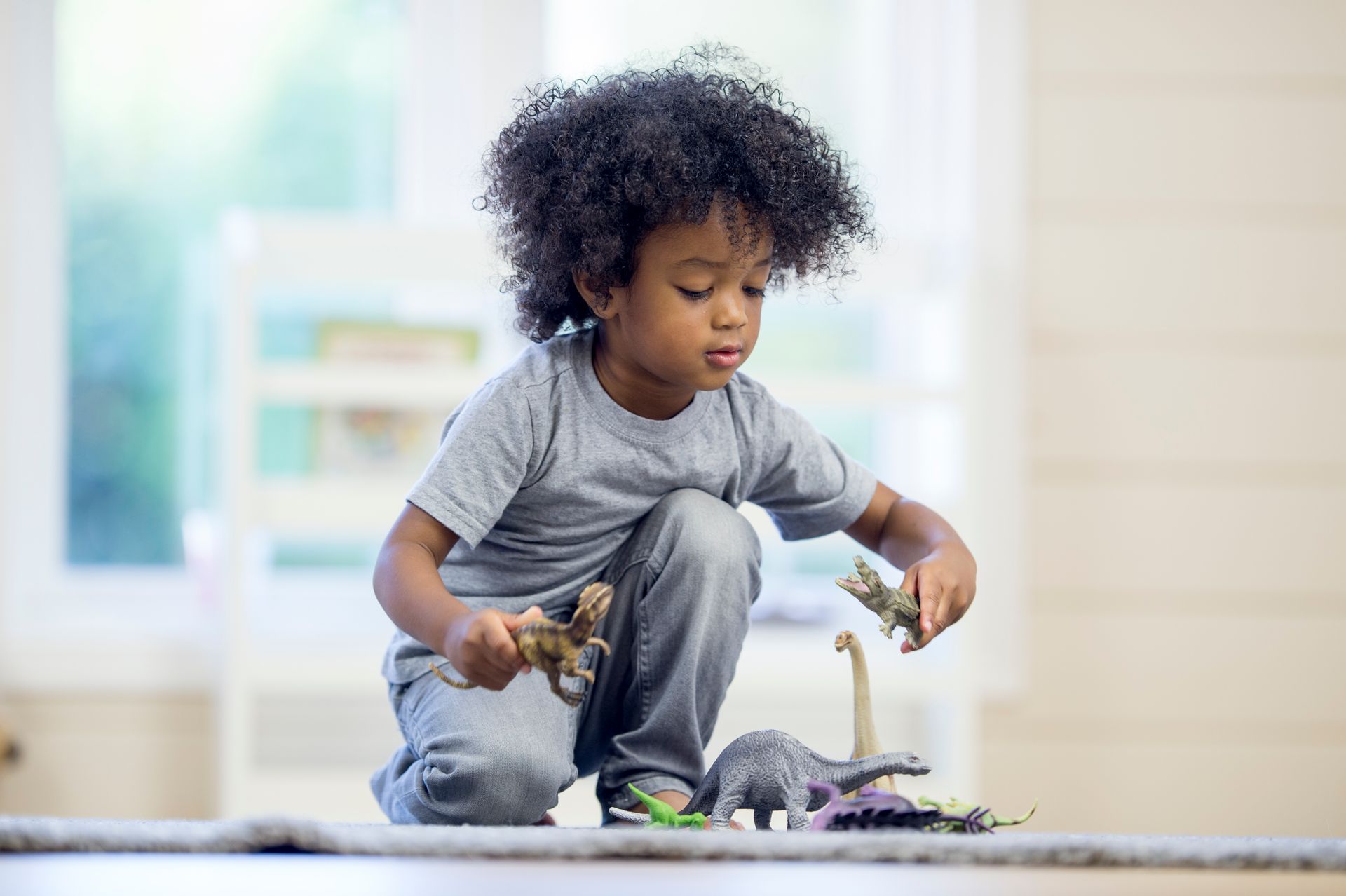 Little boy playing with dinosaur figure on a rug.