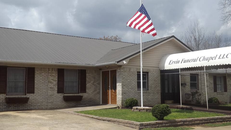 One-story brick building with an American flag and a sign above the entrance under a cloudy sky