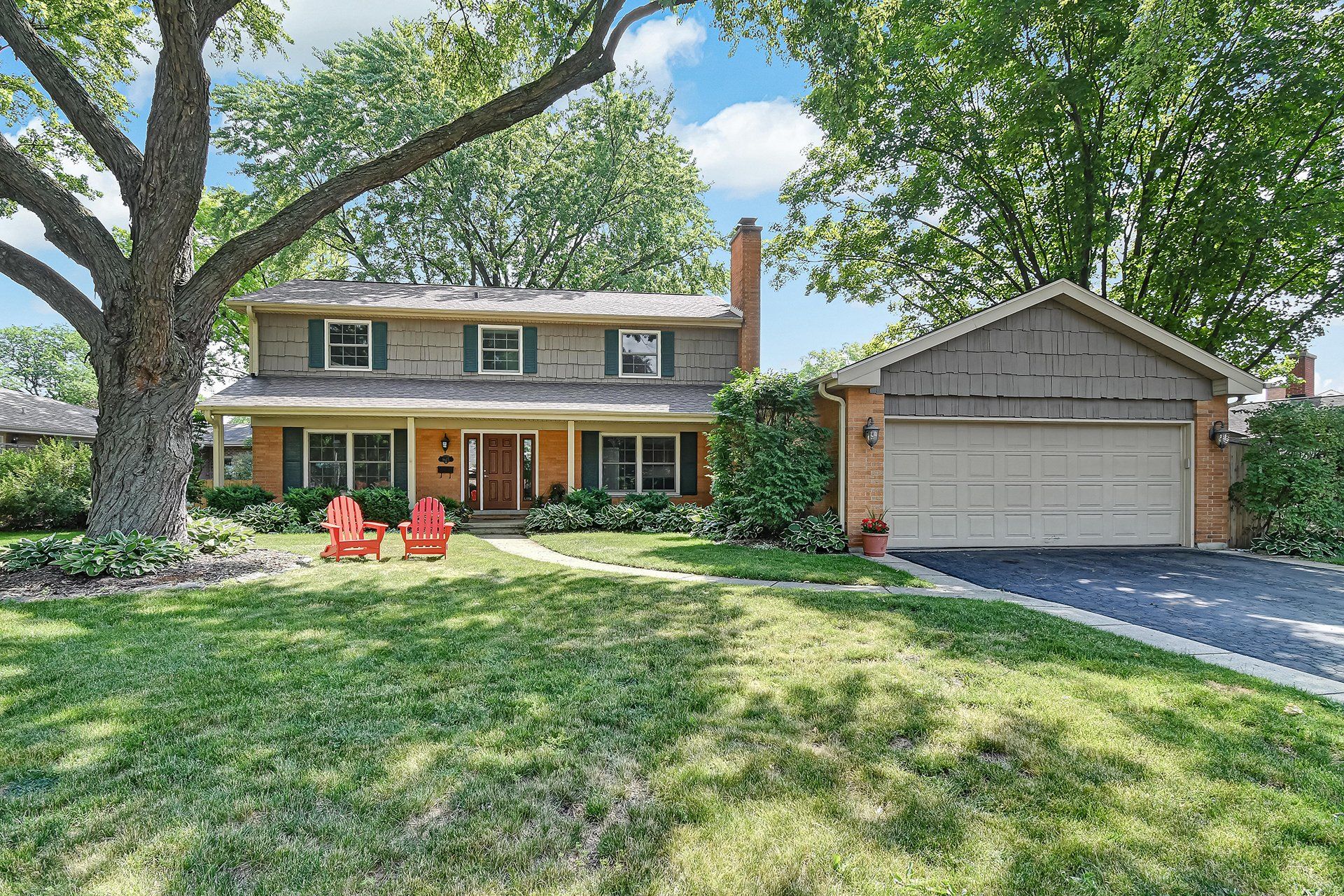A large house with a large garage and two red chairs in front of it.