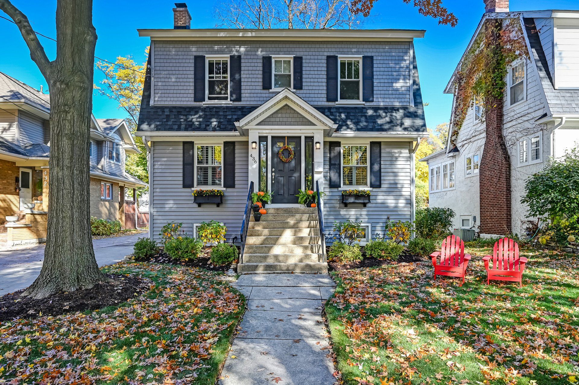 A gray house with black shutters and red chairs in front of it.