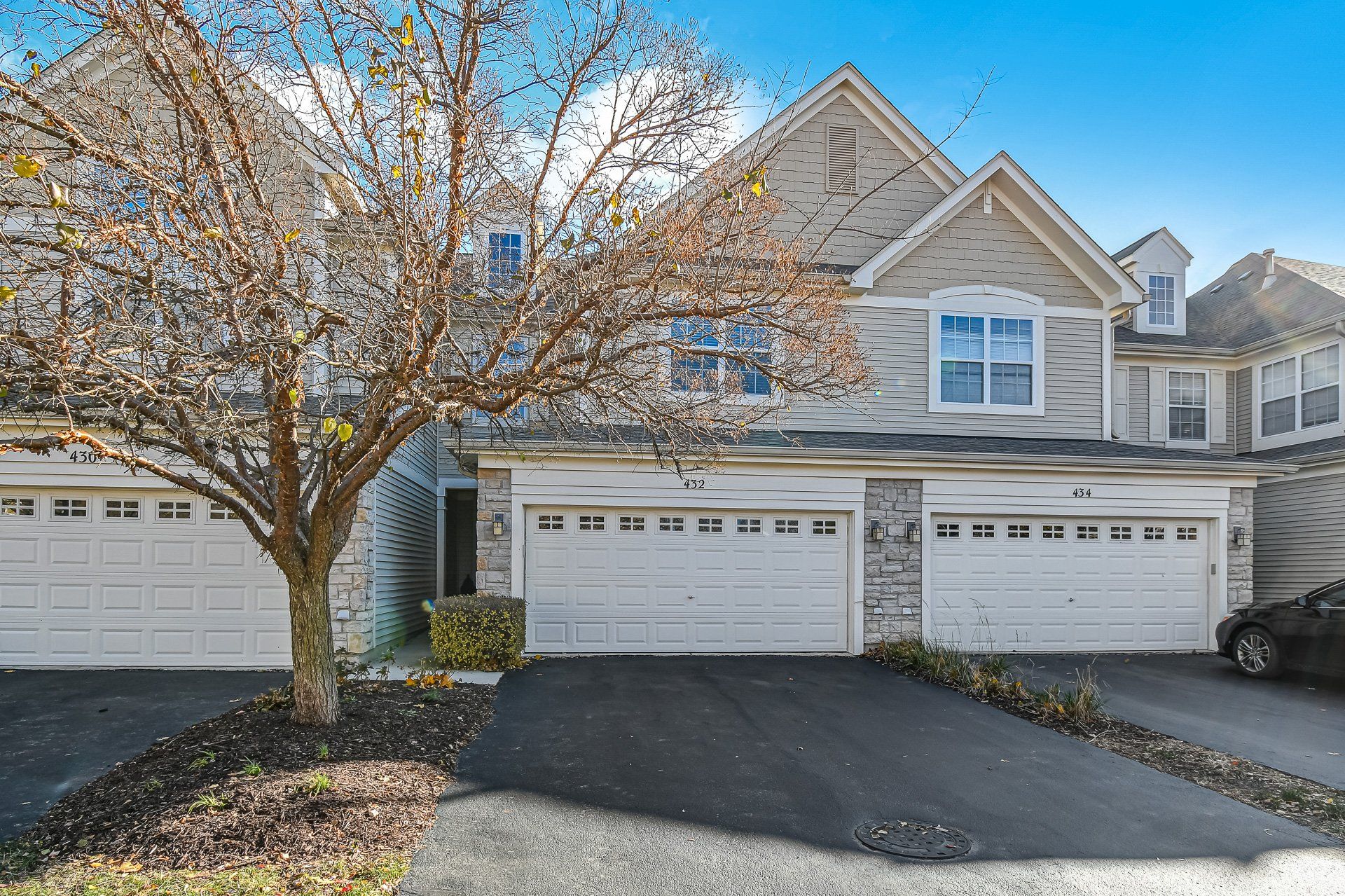 A large house with two garages and a tree in front of it.