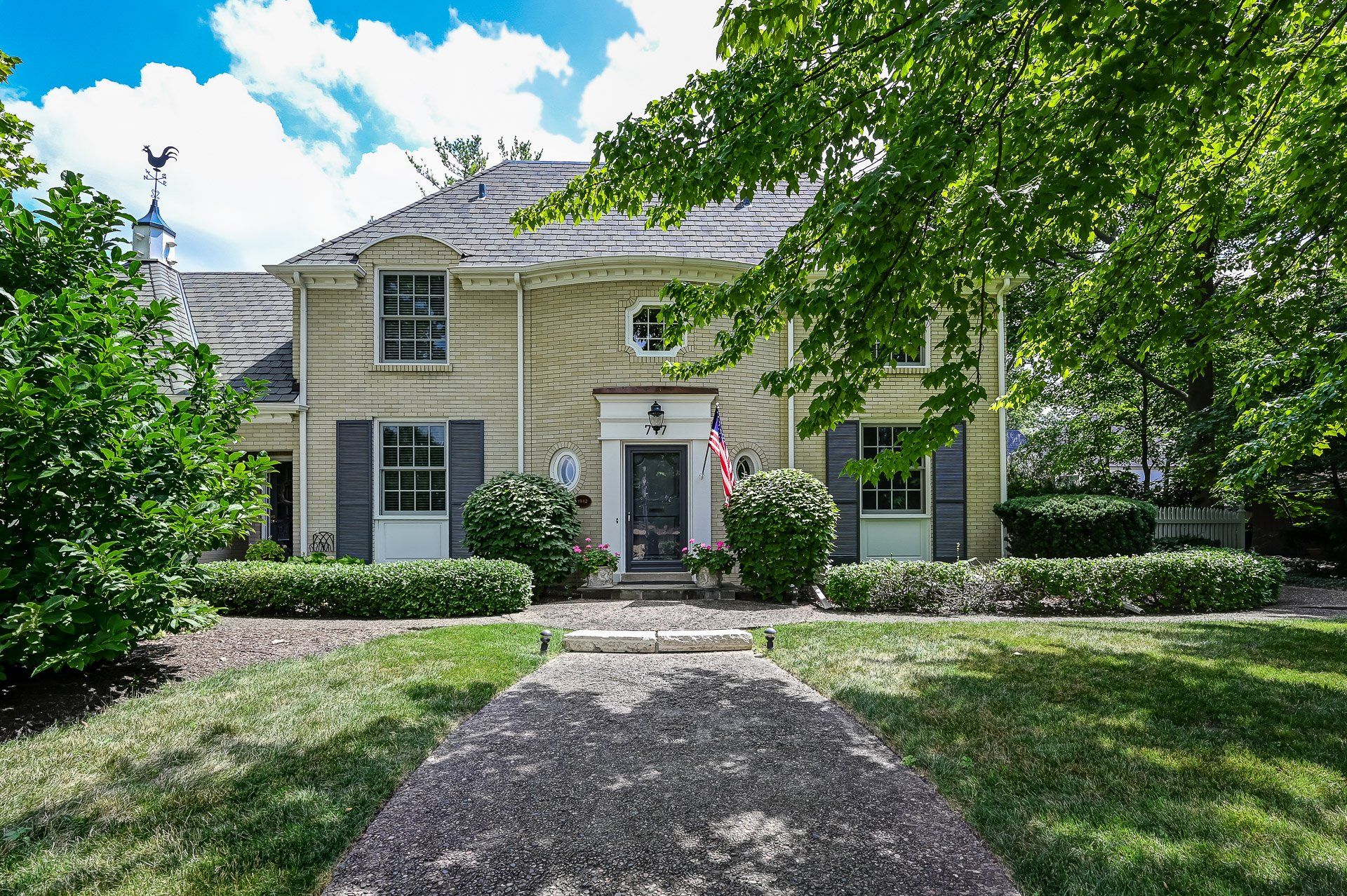 A large house with a gravel driveway leading to it is surrounded by trees and bushes.