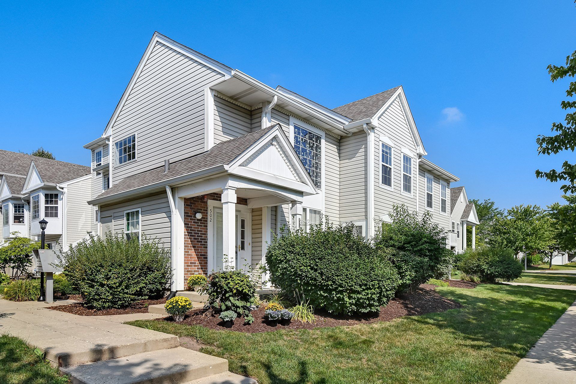 A large white house with a gray roof is sitting on top of a lush green lawn.