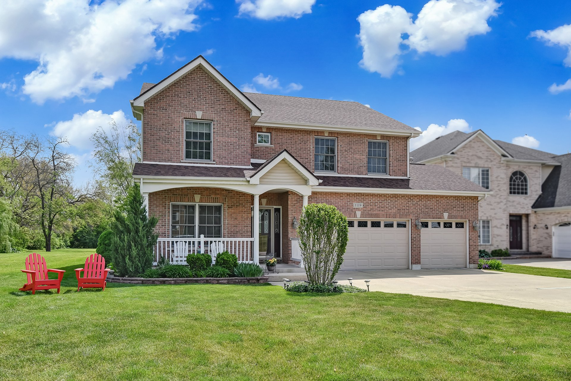 A large brick house with a porch and two red chairs in front of it.