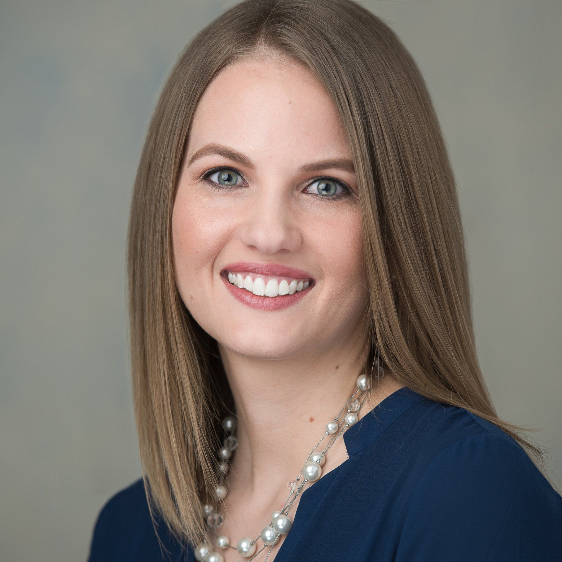 A woman wearing a blue shirt and a pearl necklace smiles for the camera