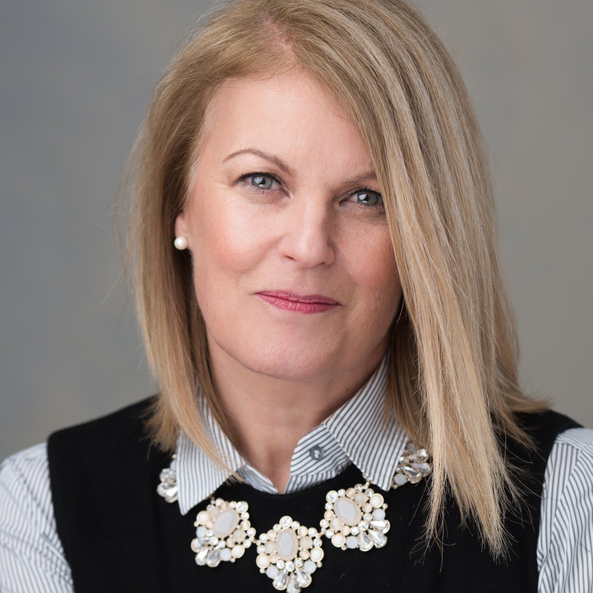 A woman with blonde hair is wearing a black vest and a necklace