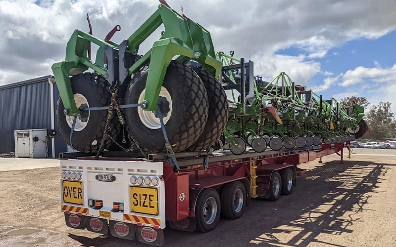 Large green farming equipment secured on a transport trailer, outdoors.