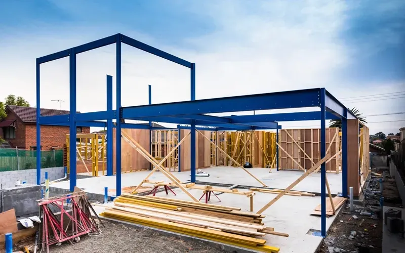 Blue steel frame of a building under construction, wooden studs, concrete foundation.